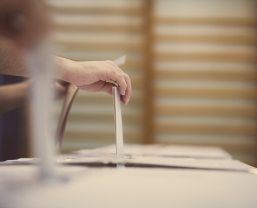 En hånd som legger en stemmeseddel i en valgurne.